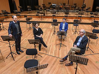 Vier Personen (Kanzler, Prorektor*in und Rektor) des Rektorats sitzen in einem leeren Orchester im Konzertsaal.