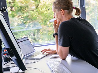 Person am Schreibtisch vor zwei PC-Bildschirmen