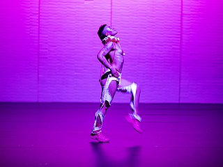 Tanzstudent*in auf der Bühne mit pinker Farbeinspielung.