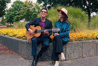 Personen mit Gitarre sitzen auf einer Bank