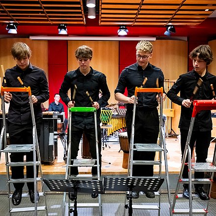 Tag der Landesjugendensembles NRW Vier Personen spielen mit Schlagstöcken auf Trittleitern